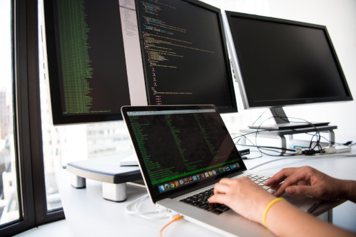 Shallow focus photo of person using MacBook and two external screens.