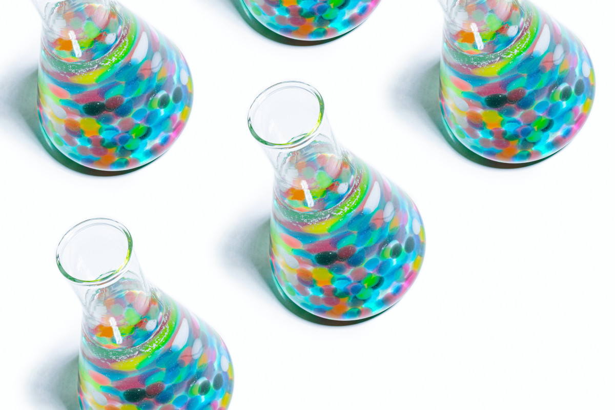 Five clear glass jars filles with a transparent liquid and multiple different coloured candied sweets