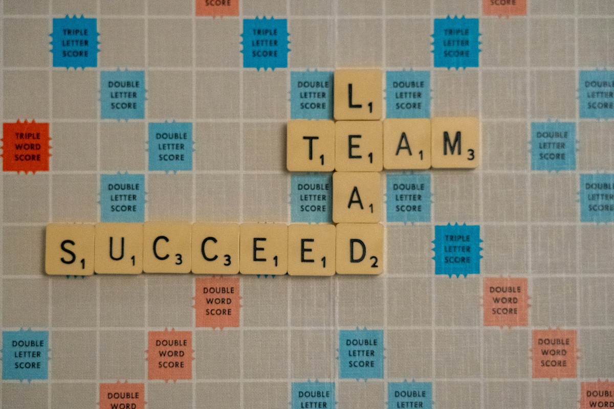 The image shows a scrabble board with words spelled out using letter tiles. The words that are chosen highlight positive and motivational themes. At the top, the word 'TEAM' is completed with three double-letter tiles, making it the longest word across that row. Below it, the word 'SUCCESS' follows, with a similar number of tiles. On the left side, the word 'LEAD' is visible. The letters on the board vary in color, with blue, green, red, yellow, and orange being used. The background of the image is not clearly visible due to the focus on the crossword puzzle. There are no people or other significant objects within the frame of the photograph.