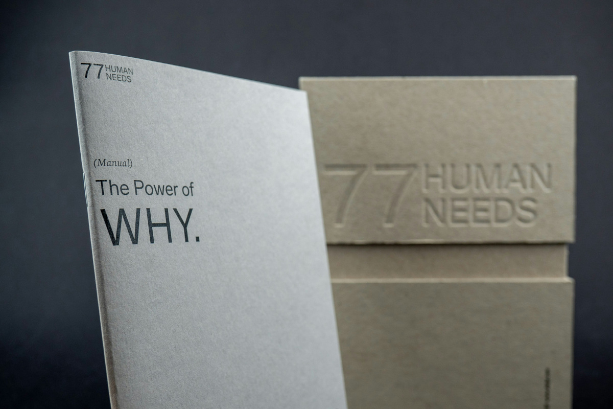 The image shows a book with the title '77 Human Needs.' The book is placed on a surface and appears to have a simple design. On the left side of the book, there's a logo that says 'The Power of Why.'