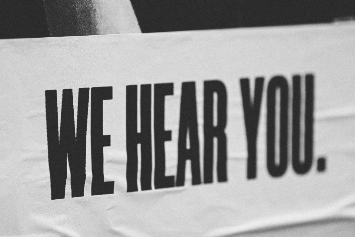 A black and white image of a banner with the text 'WE HEAR YOU.' in black text on a white banner.