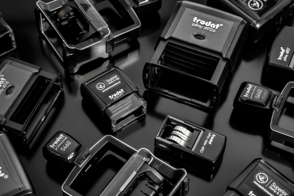 This is an image showcasing a collection of self-inking stamps. These stamps typically have a mechanical mechanism that allows them to print the same text or mark repeatedly without the need to be recharged or refilled with ink. The stamps vary in size, shape, and design, indicating they may serve different purposes for stamping documents or packaging items. Some stamps are more prominent than others.