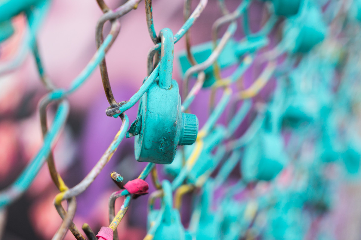 A teal coloured padlock on chain link fence.