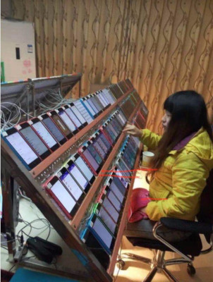 A photo of a woman in a yellow jacket, sitting in front of three rows of iPhones. There are around 70+ iPhones in front of her, and she is interacting with one of them.