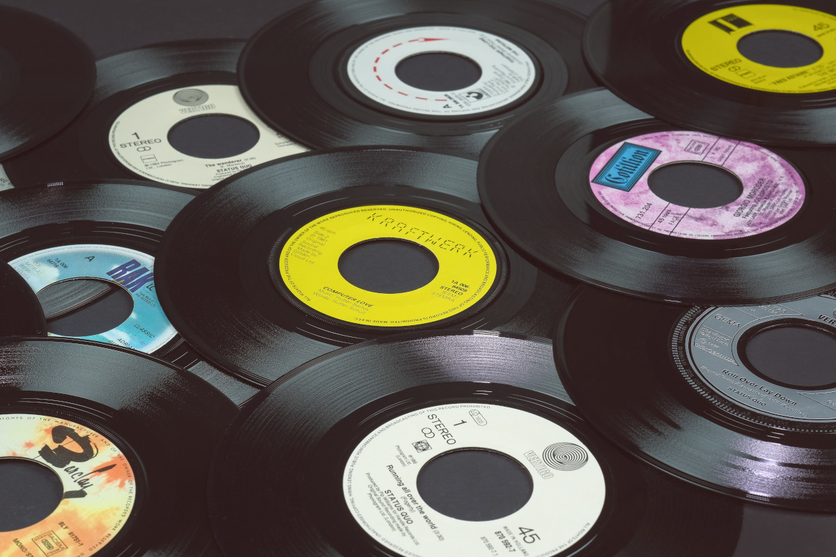A selection of black vinyl records, they are not arranged in any order and are spread out over the image, some overlapping others. Most of the records have central record label stickers, and are all in primary colours or have single colour patterns.