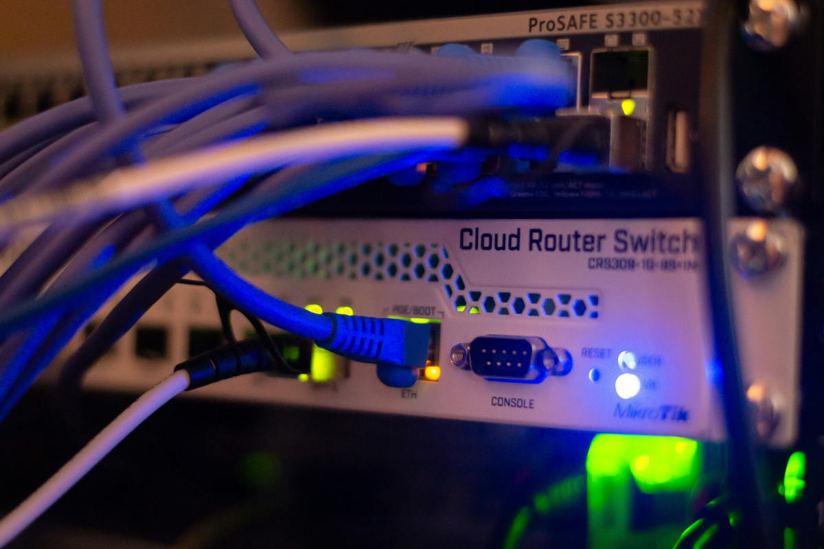 A close up photo of a piece of computer networking equipment with the legend 'CLOUD ROUTER SWITCH' across it's top right-hand side. There a number of different networking cables plugged into the device, and it's face plate is painted white.
