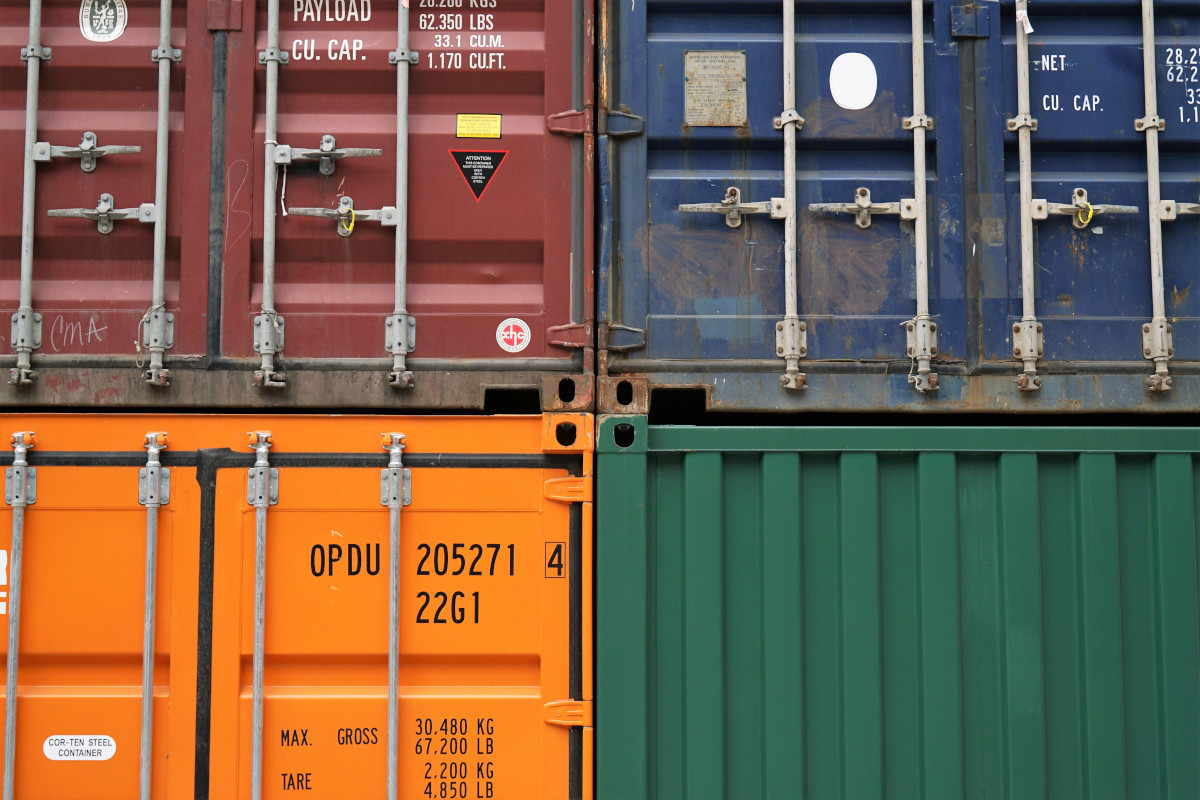 Four cargo containers arranged on top of each other. The containers are each coloured differently, from top to bottom and left to right they are: red, blue, orange, and green
