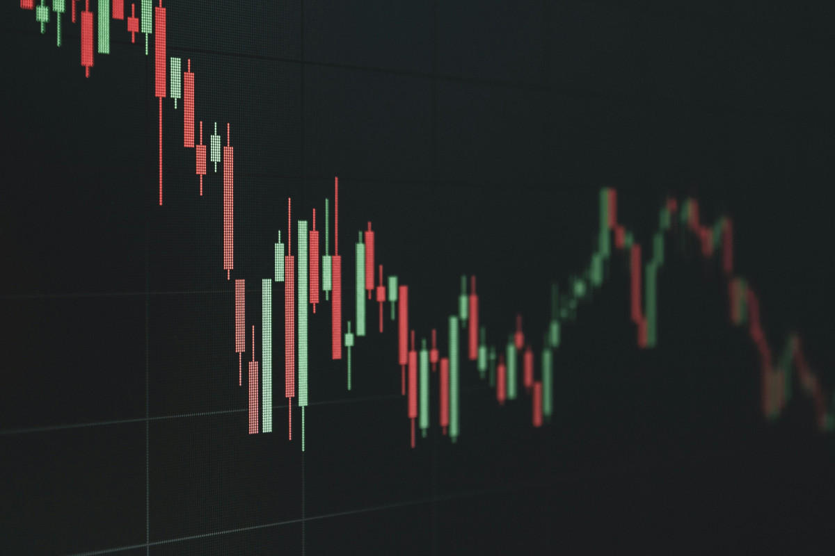 The image displays a computer screen showing a trading chart with various indicators and candlestick patterns. The chart is set against a dark background, which helps the colors of the chart stand out. The candlesticks represent price movements within certain time frames, often used in technical analysis to predict future market behaviour. The trading chart includes what appears to be a Fibonacci retracement tool, which is used by traders to identify potential levels of support and resistance based on past price actions. There are also other technical indicators visible, such as a moving average and possibly a volume indicator or another custom indicator on the lower part of the screen. The chart's design suggests that it could be part of a trading platform used by a trader to analyze the financial markets, possibly for stocks, currencies, commodities, or other tradable instruments. The presence of candlesticks and multiple indicators indicates that the user is likely performing technical analysis to inform their trading decisions. The image itself is a digital composition with no real-world context provided. It is meant to convey a concept related to financial trading and chart analysis rather than depict a specific event or location.