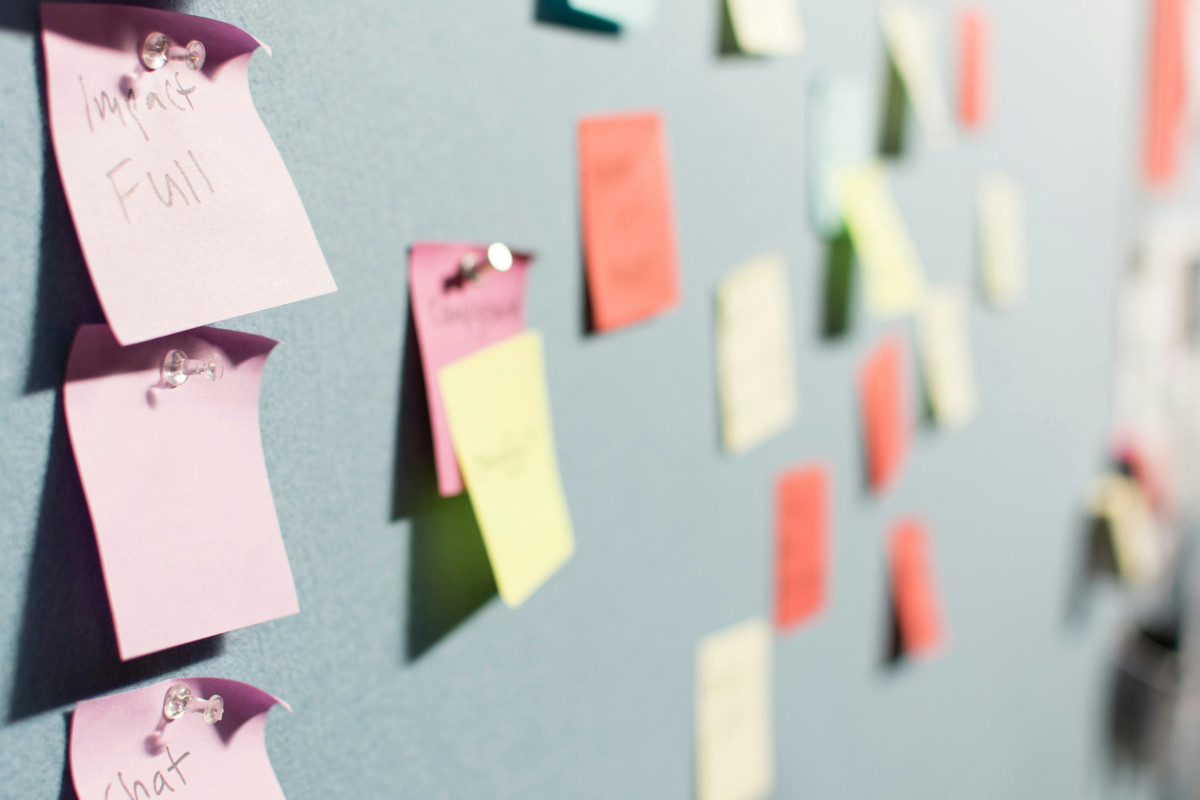 A number of coloured sticky notes are arranged on a pinboard. The sticky notes do have handwritten text on them, but they are out of focus, meaning that the text is unreadable