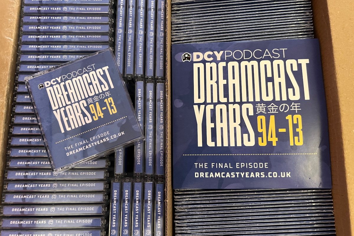 An open cardboard box, containing physical copies of both the CD and MiniDisc versions of the final episode of the Dreamcast Years podcast. On the left is a collection of the MiniDisc version, and on the right is a collection of the CD version. Both have blue cases which bear the legend 'DCY Podcast Dreamcast Years 黄金の年' in a white font, with '94-13' in a yellow font alongside it, and 'The final episode dreamcastyears.co.uk' along the bottom. The Japanese text '黄金の年' can be translated to me 'golden years' and is read 'kogane no toshi'.