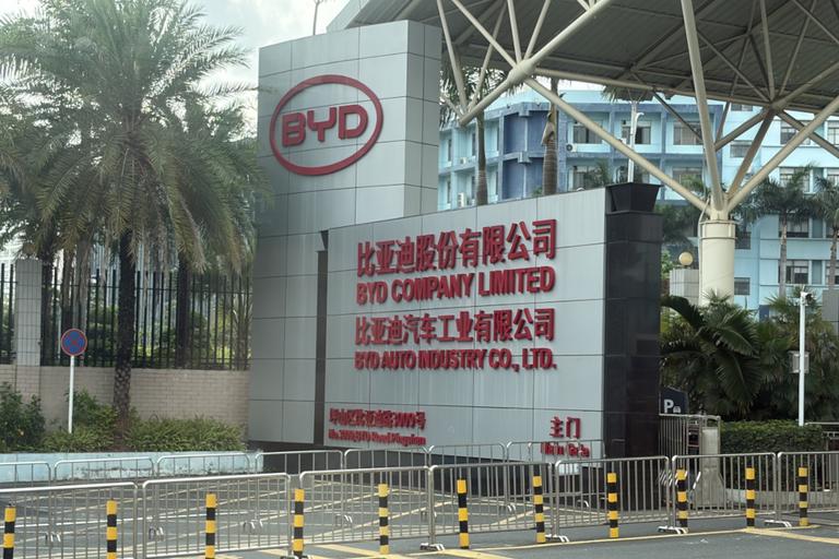 A road side sign for BYD's headquarters. It reads 'BYD COMPANY LIMITED, BYD AUTO INDUSTRY CO, LTD.'in all caps, red text against a white background.
