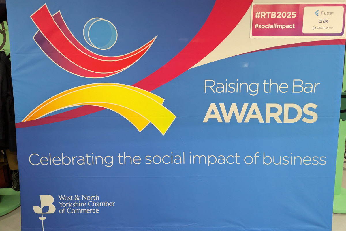 A vibrant banner adorned with a colourful graphic design that prominently features the logo of both the West and North Yorkshire Chamber of Commerce's prestigious Raising The Bar Awards and the logos of corporate sponsors for the event. The banner proudly announces the 'Raising the Bar Awards,'' which are celebrating the social impact of businesses in the region.